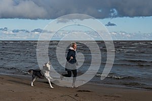 A girl with a husky dog Ã¢â¬â¹Ã¢â¬â¹runs on the beach on Lake Peipus on an autumn day photo